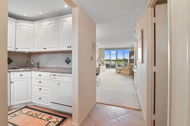 kitchen with white dishwasher, sink, white cabinets, and light tile patterned flooring