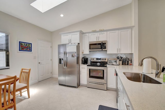 kitchen with sink, stainless steel appliances, vaulted ceiling with skylight, white cabinets, and light tile patterned floors