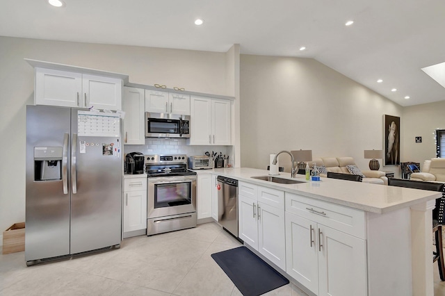 kitchen featuring kitchen peninsula, sink, vaulted ceiling, white cabinetry, and appliances with stainless steel finishes