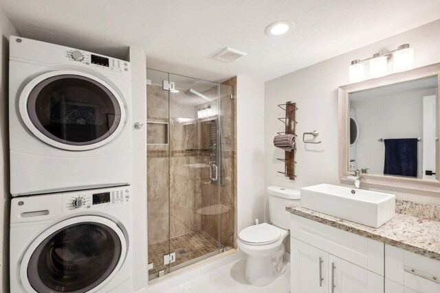 interior space with a shower with door, stacked washing maching and dryer, vanity, and toilet