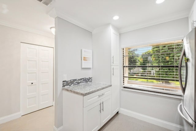 kitchen featuring white cabinetry, crown molding, stainless steel refrigerator, and light stone countertops