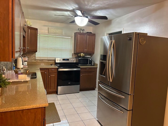 kitchen with light tile patterned floors, stainless steel appliances, light stone counters, ceiling fan, and decorative backsplash