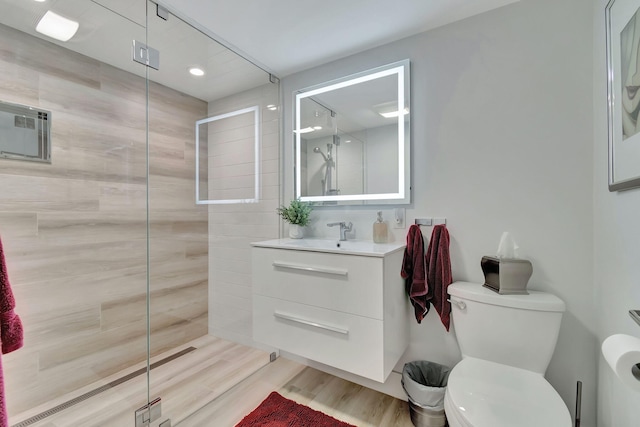 bathroom featuring a tile shower, vanity, toilet, and wood-type flooring