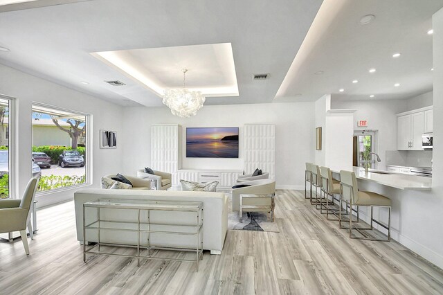 living room featuring an inviting chandelier, light hardwood / wood-style floors, a raised ceiling, and sink