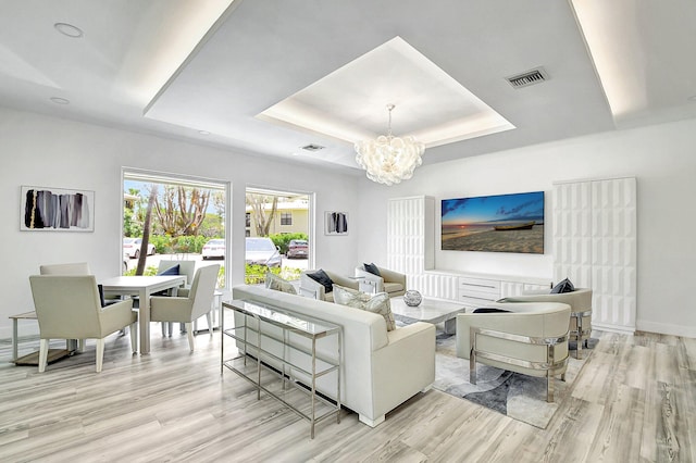 living room with a raised ceiling, a chandelier, and light hardwood / wood-style flooring