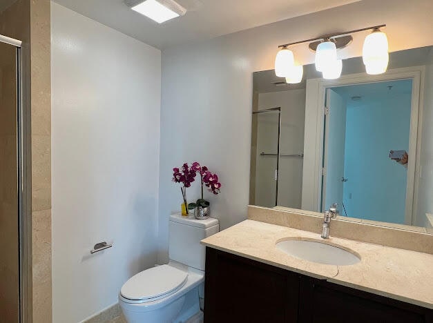 bathroom with a shower with shower door, toilet, and vanity