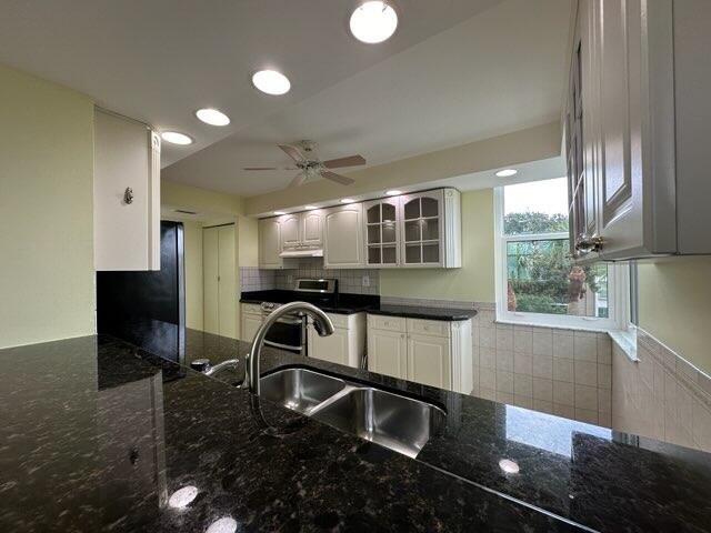 kitchen featuring ceiling fan, dark stone counters, white cabinetry, and range