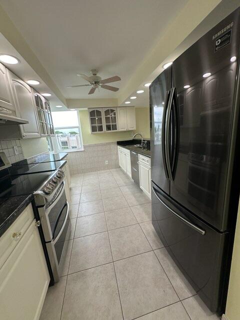 kitchen featuring appliances with stainless steel finishes, decorative backsplash, white cabinets, light tile patterned floors, and ceiling fan