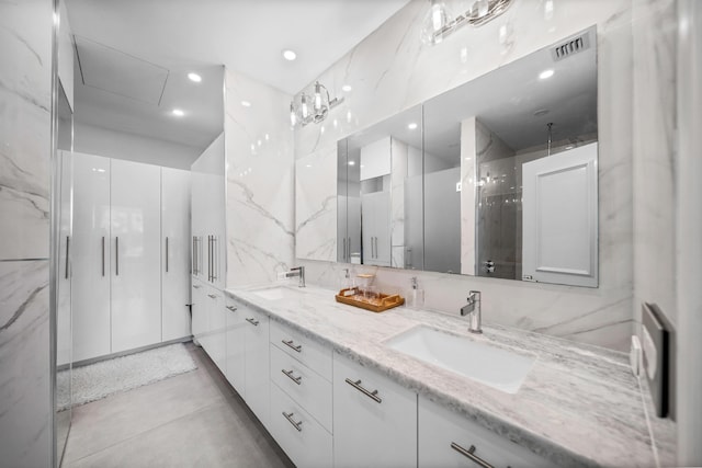 bathroom featuring a sink, a marble finish shower, visible vents, and double vanity