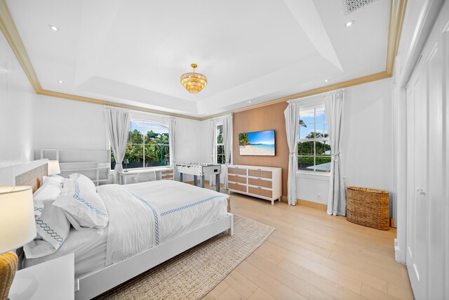 bedroom featuring a raised ceiling, light wood-type flooring, ornamental molding, and multiple windows