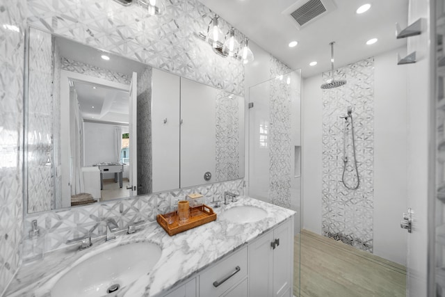 bathroom featuring a sink, visible vents, tiled shower, and double vanity