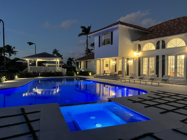 pool at dusk featuring an in ground hot tub, french doors, a patio area, and a gazebo