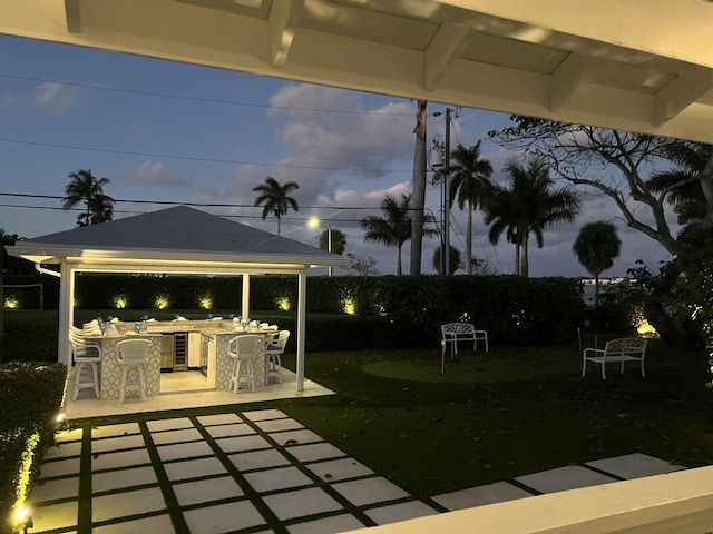 patio terrace at dusk featuring a gazebo, an outdoor kitchen, and an outdoor bar