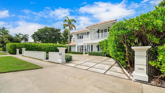 mediterranean / spanish-style home featuring stucco siding, a fenced front yard, concrete driveway, a balcony, and a tiled roof