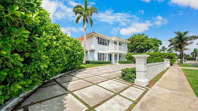 view of front of home featuring stucco siding, driveway, a fenced front yard, a balcony, and a tiled roof