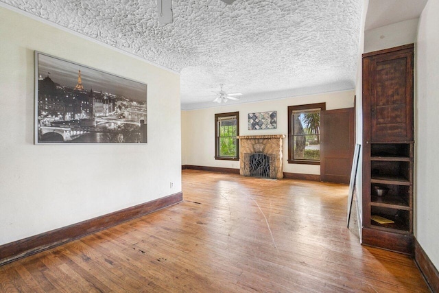 unfurnished living room featuring a textured ceiling, a stone fireplace, ceiling fan, and hardwood / wood-style flooring