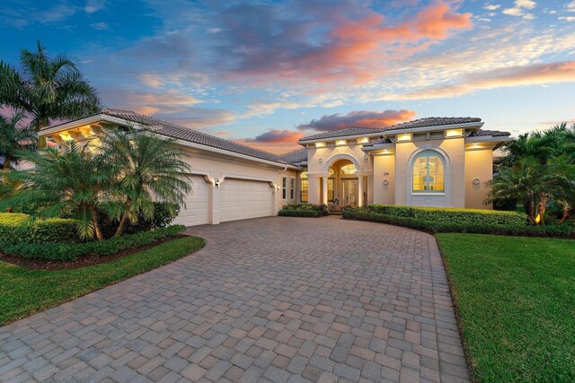 mediterranean / spanish home with a garage, a tiled roof, a yard, decorative driveway, and stucco siding