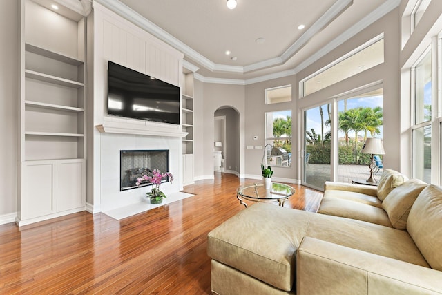 living room featuring light wood-type flooring, a towering ceiling, ornamental molding, and built in shelves