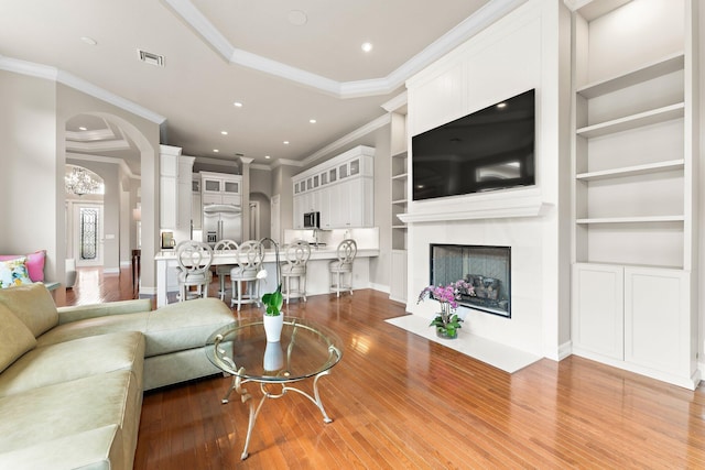 living room with ornamental molding, built in shelves, light hardwood / wood-style floors, a tray ceiling, and a high end fireplace