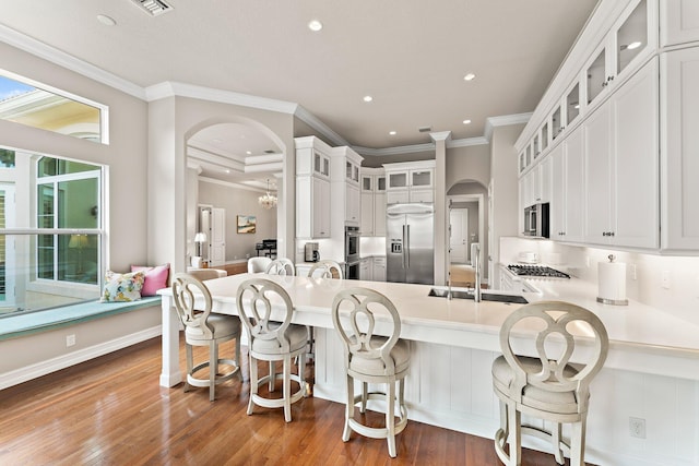 kitchen with hardwood / wood-style floors, ornamental molding, white cabinetry, appliances with stainless steel finishes, and sink