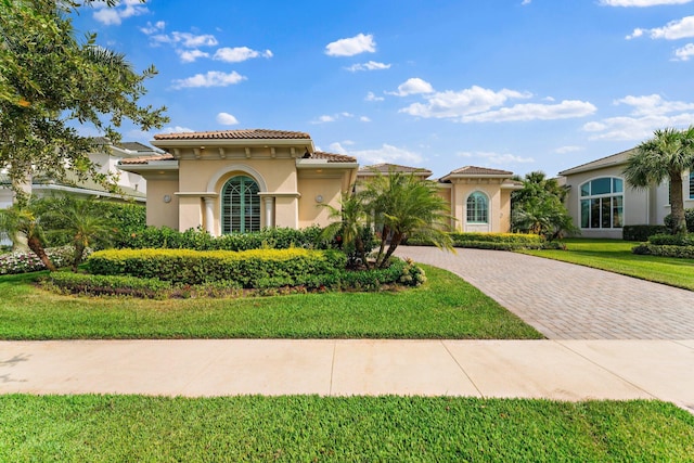 mediterranean / spanish house featuring stucco siding, a tiled roof, decorative driveway, and a front yard