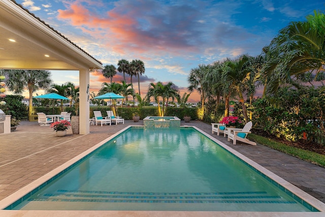 pool at dusk featuring an in ground hot tub and a patio