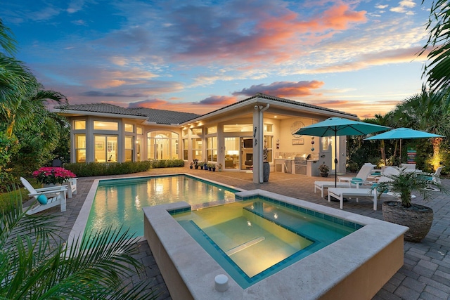 pool at dusk with an in ground hot tub and a patio