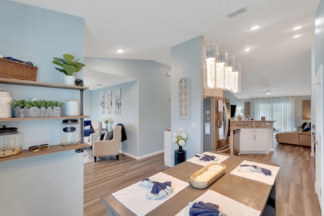 dining room featuring ceiling fan with notable chandelier, lofted ceiling, sink, and light hardwood / wood-style flooring