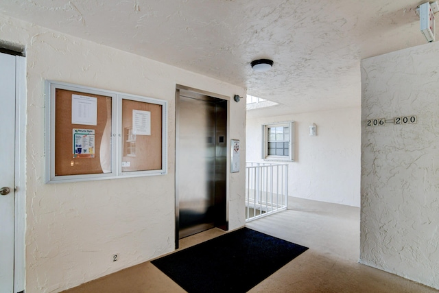 corridor featuring elevator, a textured wall, and a textured ceiling