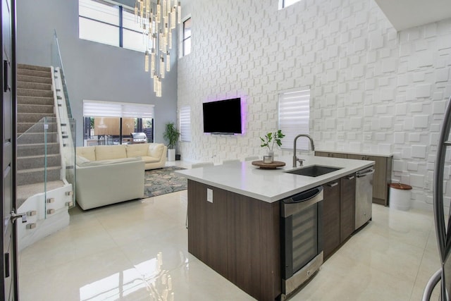 kitchen with an inviting chandelier, dark brown cabinetry, a high ceiling, sink, and a center island with sink