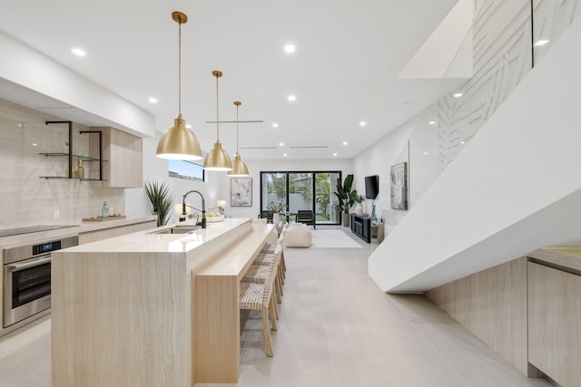 kitchen featuring oven, light brown cabinetry, hanging light fixtures, sink, and a large island