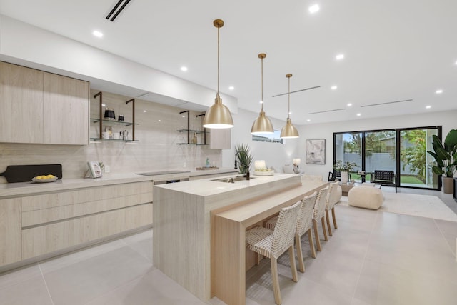 kitchen with backsplash, sink, hanging light fixtures, a center island with sink, and light brown cabinets