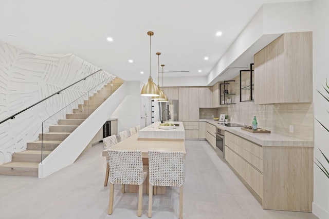 kitchen featuring backsplash, a kitchen island with sink, hanging light fixtures, sink, and stainless steel oven