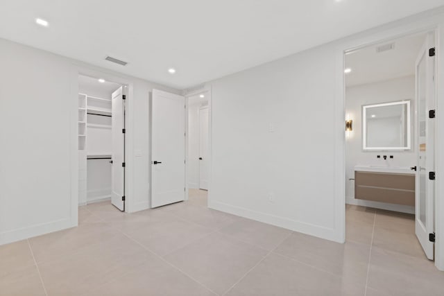 unfurnished bedroom featuring a closet, light tile patterned floors, a spacious closet, and ensuite bath