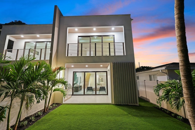 back house at dusk featuring a lawn