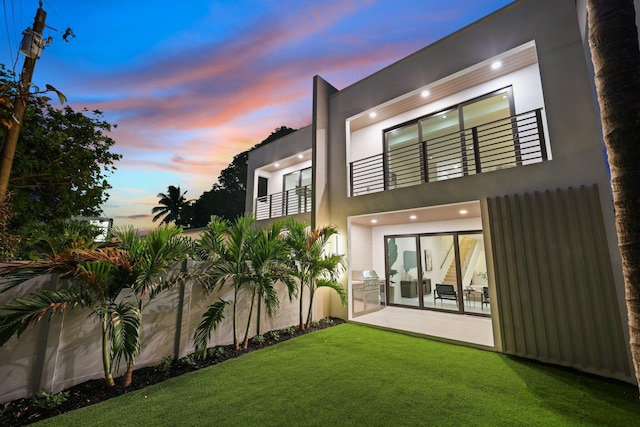 back house at dusk with a lawn and a patio