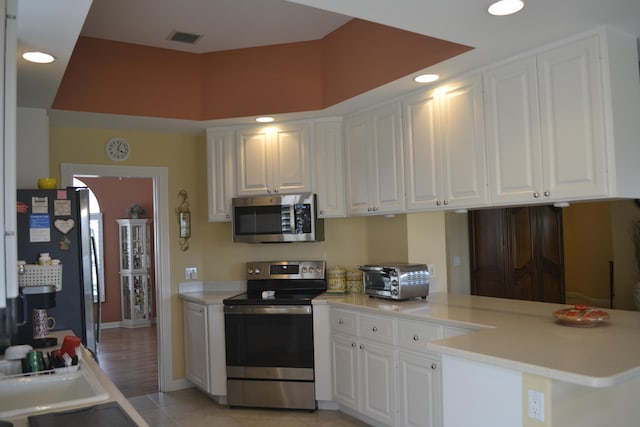 kitchen featuring light tile patterned floors, stainless steel appliances, kitchen peninsula, and white cabinets