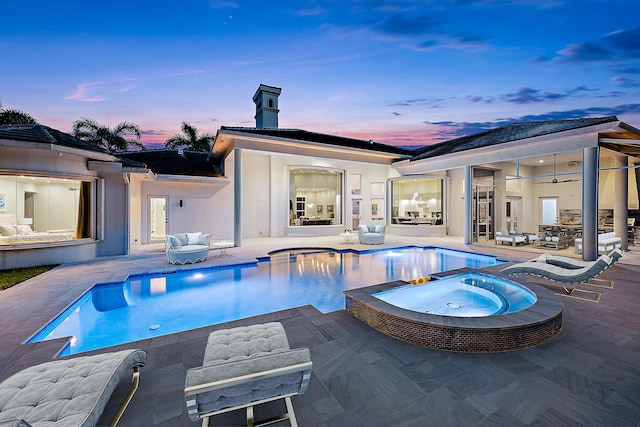 pool at dusk featuring an in ground hot tub and a patio area