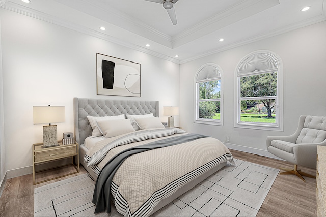 bedroom featuring light wood-type flooring, crown molding, ceiling fan, and a tray ceiling