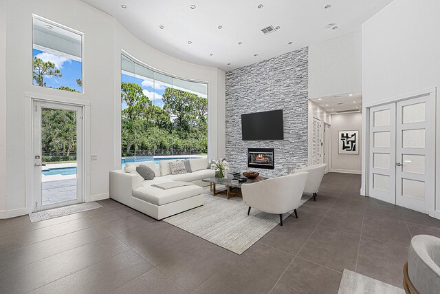 living room featuring a towering ceiling, a stone fireplace, dark tile patterned floors, and a healthy amount of sunlight