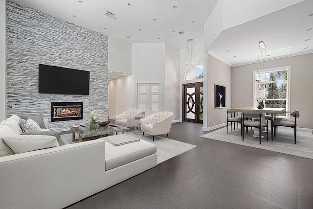 living room with a stone fireplace, a towering ceiling, and crown molding