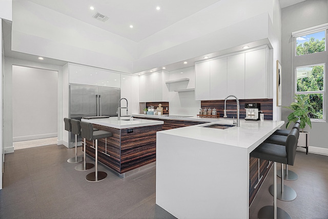 kitchen with an island with sink, a towering ceiling, sink, and a kitchen breakfast bar