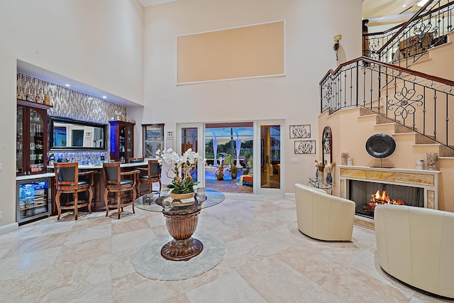 foyer entrance featuring a dry bar, a towering ceiling, beverage cooler, a warm lit fireplace, and stairs