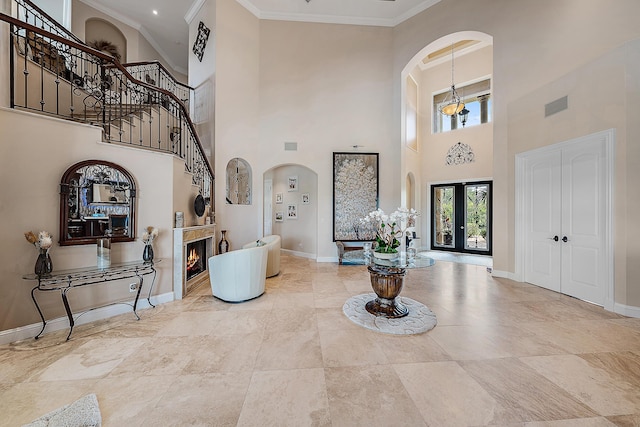 foyer entrance featuring baseboards, arched walkways, ornamental molding, a lit fireplace, and french doors