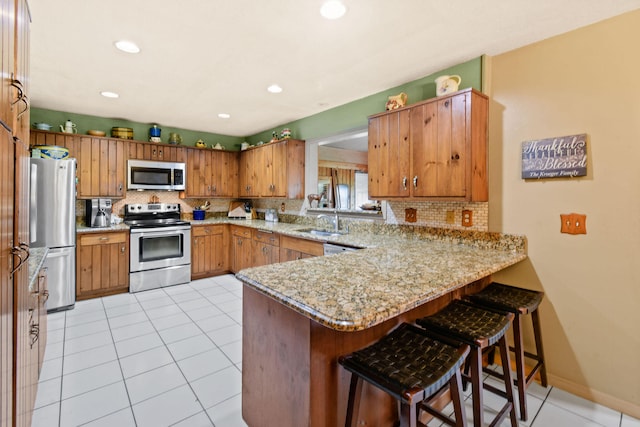 kitchen with stainless steel appliances, a kitchen breakfast bar, kitchen peninsula, light tile patterned flooring, and light stone counters