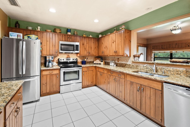 kitchen featuring stainless steel appliances, decorative backsplash, light tile patterned flooring, light stone counters, and sink