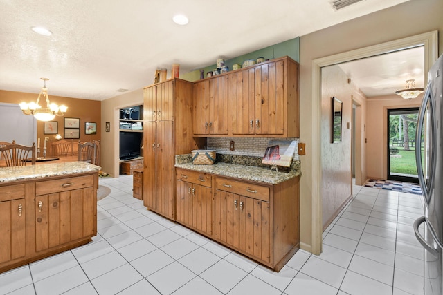 kitchen featuring stainless steel fridge, a notable chandelier, light stone counters, and pendant lighting