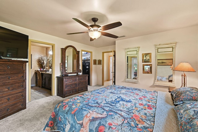 bedroom with ceiling fan, light colored carpet, and ensuite bath