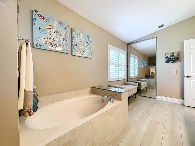 bathroom with vaulted ceiling, a relaxing tiled tub, and tile patterned floors