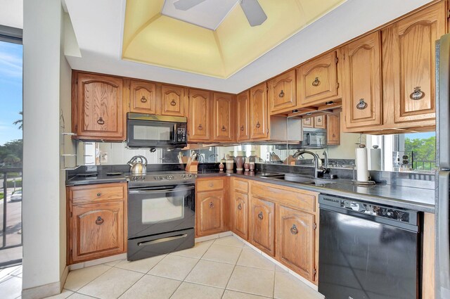 kitchen with black appliances, light tile patterned floors, a tray ceiling, sink, and ceiling fan